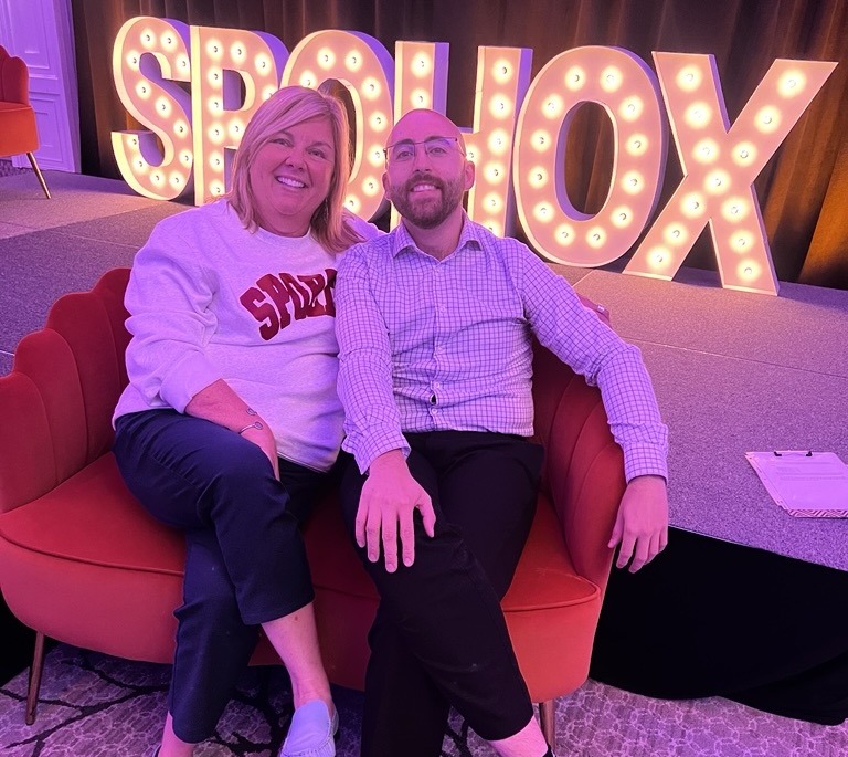 Liam seated with a guest in front of the SPOHOX sign